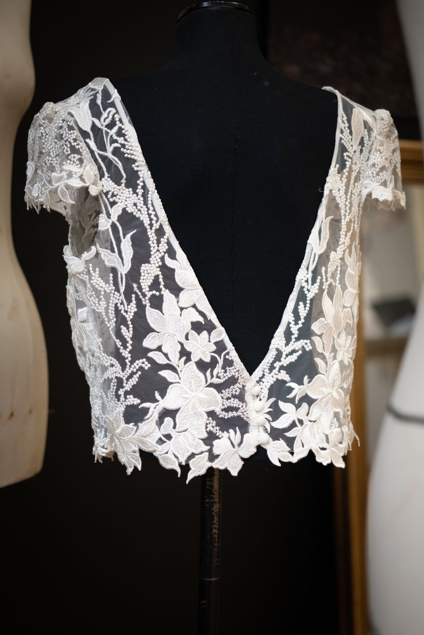 Grand décolleté dos, application de motifs cousus mains pour la finition du bas. Tulle brodé Stragier.